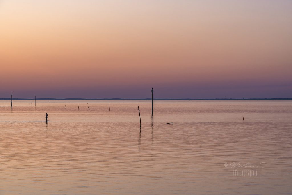 Silhouette d'une femme marchant dans l'eau à marée basse au coucher du soleil, Bassin d'Arcachon