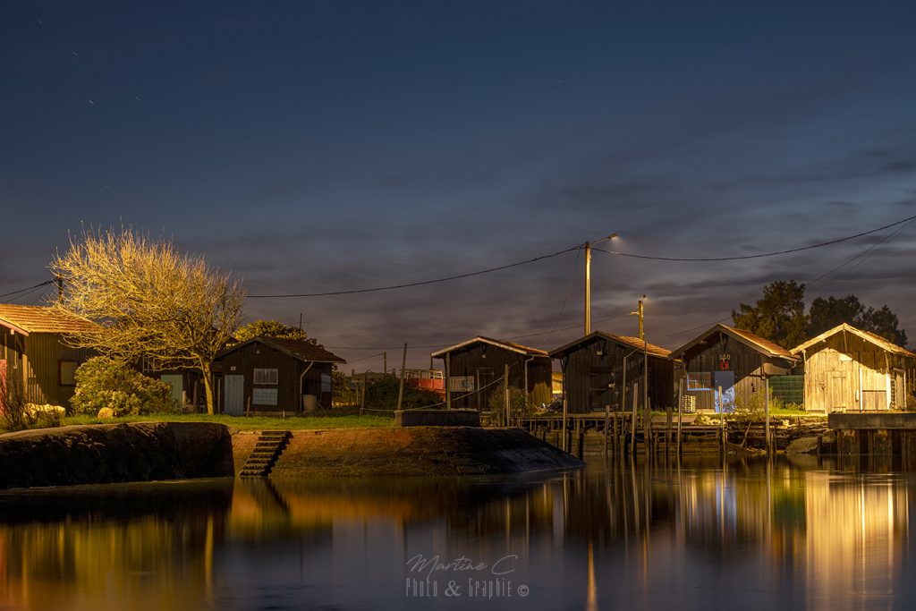 Port du Canal à Gujan-Mestras de nuit, cabanes et lumières reflétées dans l'eau