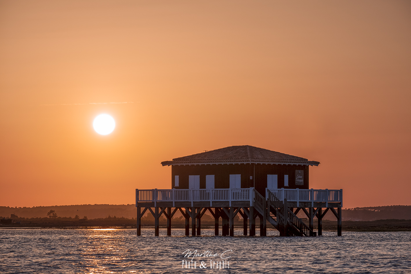 Ciel orange avant le coucher du soleil aux cabanes Tchanquées à marée haute, Bassin d'Arcachon